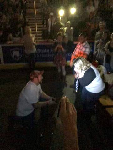 A man down on one knee proposing to an ecstatic women at a concert